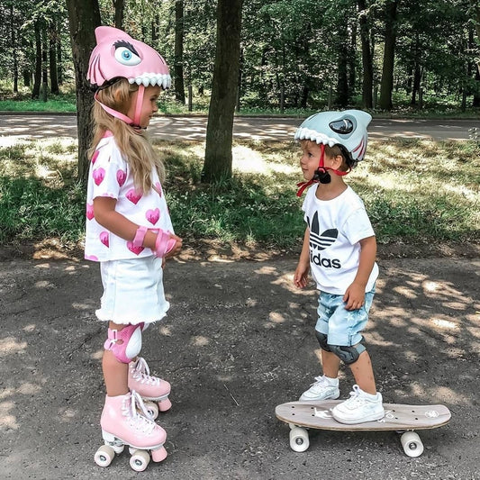 Kids enjoying outdoor fun wearing Crazy Safety helmets, featuring the blue 3D Shark helmet on a skateboarder and pink roller skates with a matching helmet, perfect for safe and playful adventures.